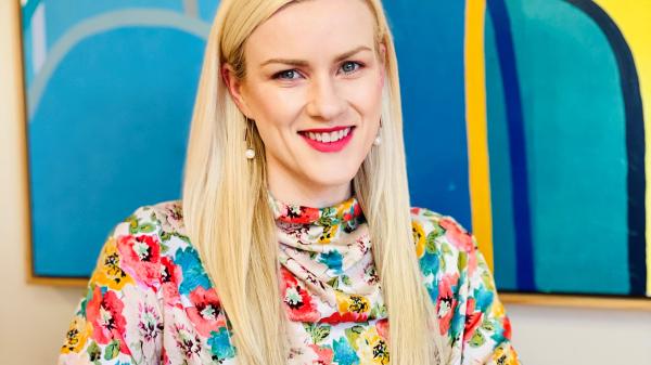 Richelle McCausland sits with her arms folded in front of a bright image