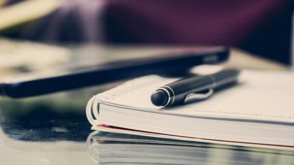 A binder notebook sits on a desk with a black pen on top