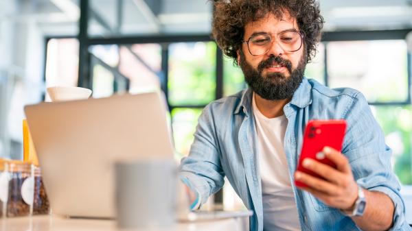 A man with curly hair smiles slightly at a red mobile phone in his hand