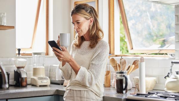 A woman surveys her phone leaning against a corner in a breezy kitchen