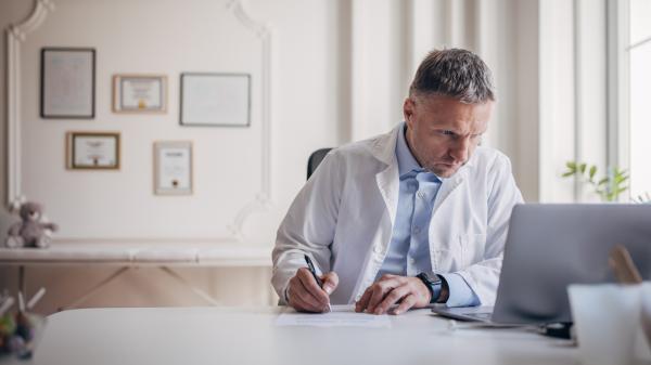 A man stares in concentration at a computer screen wearing a white lapcoat