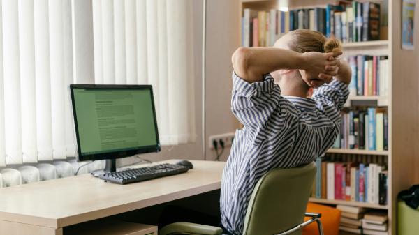 Man sits back with arms behind his head staring at screen