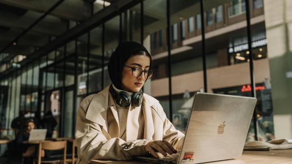 Woman with a hijab and headphones examines her computer screen