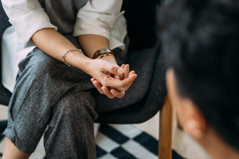 Hands are clasped on the knees of a woman in smart casual attire