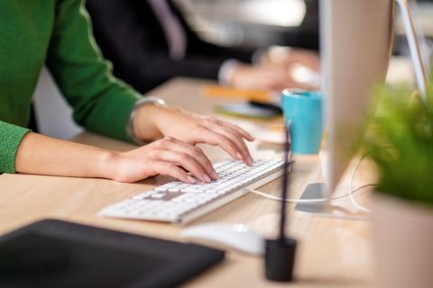 A woman in a green shirt types on a computer keyboard